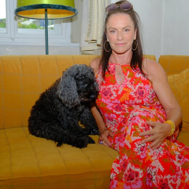Christine Neubauer sitzt mit ihrem Hund auf einer gelben Couch