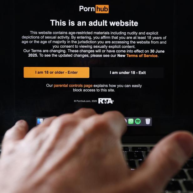 Auf einem Laptop-Bildschirm ist die Altersabfrage von Pornhub zu sehen. Eine Hand berührt die Tastatur.