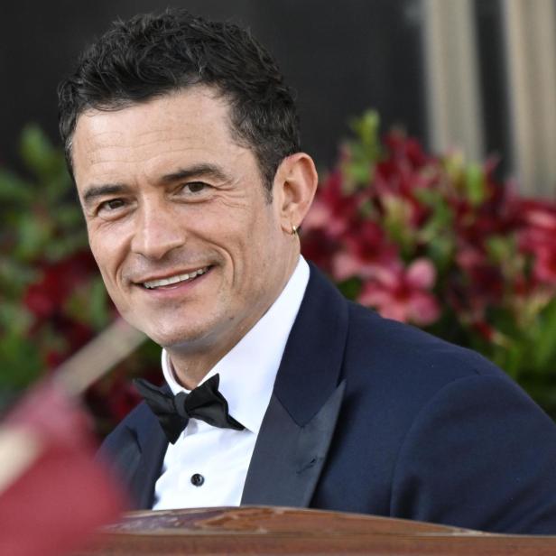Orlando Bloom lächelt in einem dunklen Anzug mit Fliege.