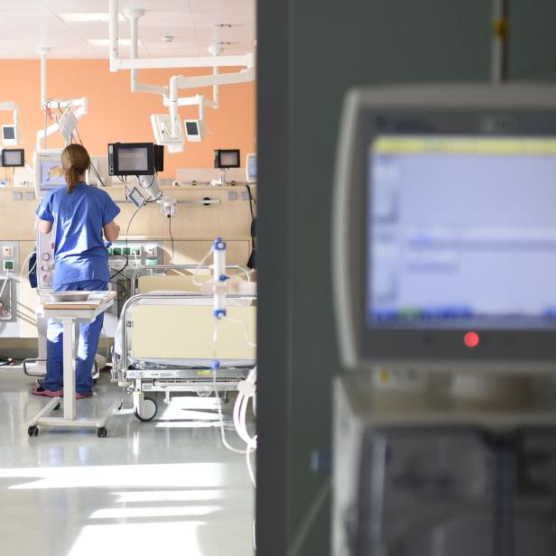 Spitalszimmer mit Monitor im Vordergrund, Betten und Pflegekraft im Hintergrund