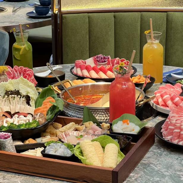 Ein Tisch reich gedeckt mit Zutaten für Hot Pot, darunter Fleisch, Gemüse und Getränke.