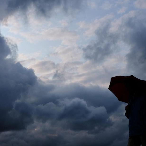 Eine Person mit einem Regenschirm vor einem dunklen, bewölkten Himmel.
