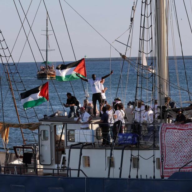 Mehrere Menschen stehen auf einem Segelschiff mit palästinensischen Flaggen, das auf dem Meer fährt.