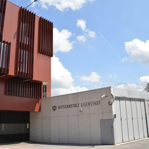 Modernes Gebäude mit roten Fassadenelementen und einem gesicherten Bereich mit Stacheldraht und Überwachungskameras.