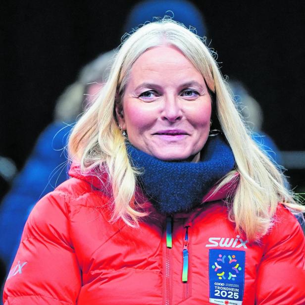Mette-Marit in roter Jacke mit dem Logo „Trondheim 2025“ blickt in die Kamera.