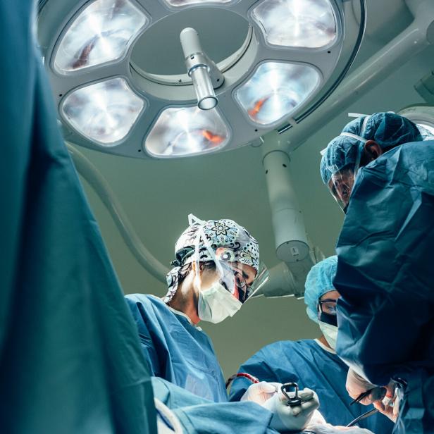 Ein OP-Team in blauer Kleidung arbeitet unter hellem Licht im Operationssaal.