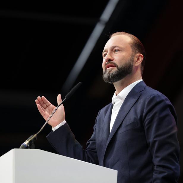 Ein Mann im Anzug spricht an einem Rednerpult mit Mikrofon und gestikulierter Hand.
