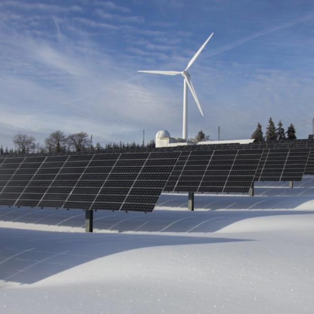 Solarpanels und Windräder stehen im Schnee, umweltfreundliche Energieerzeugung in winterlicher Landschaft.