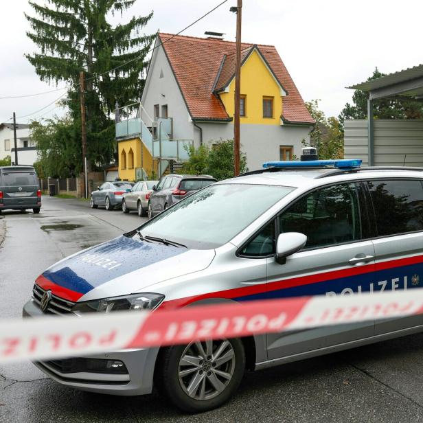 Absperrband der Polizei vor Polizeiauto, dahinter Häuser