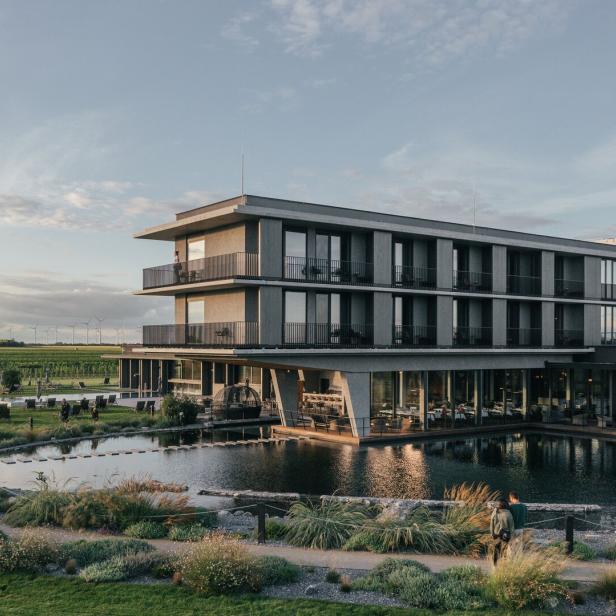 Ein modernes Hotel mit Pool liegt inmitten einer grünen Landschaft mit Weinbergen.