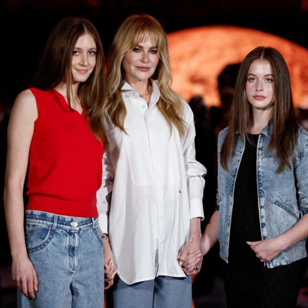 Nicole Kidman steht mit ihren Töchter Sunday und Faith Händchen haltend vor einem dunklen Hintergrund.