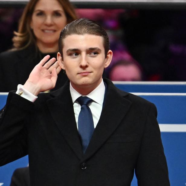 Barron Trump im dunklen Mantel hält die Hand an sein Ohr.