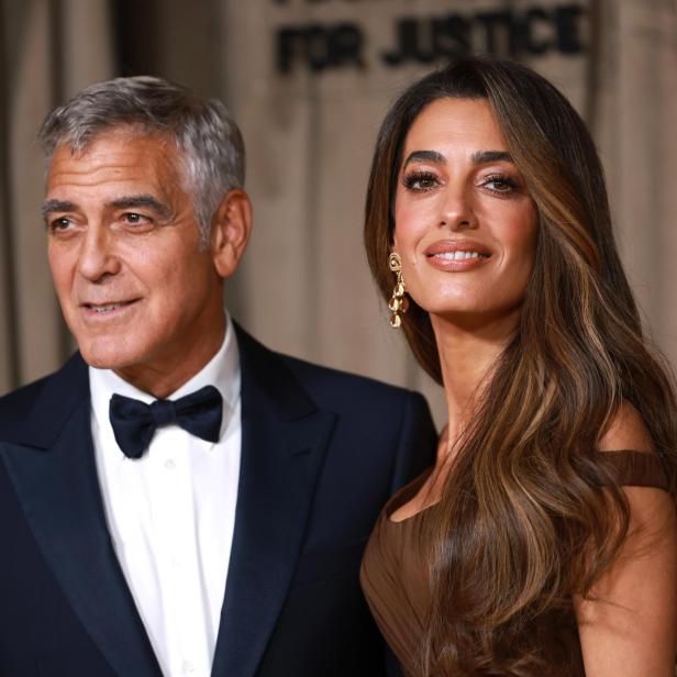 George und Amal Clooney posieren lächelnd vor einem Hintergrund mit der Aufschrift "For Justice".