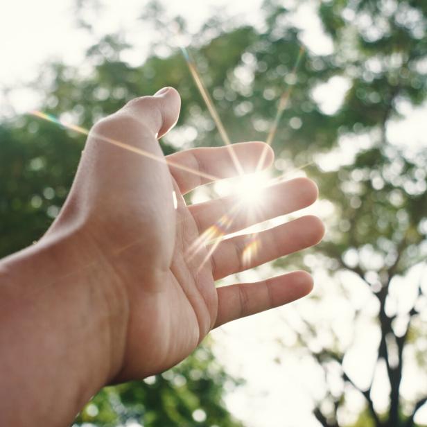 Ausgetreckte Hand, die nach der Sonne greift