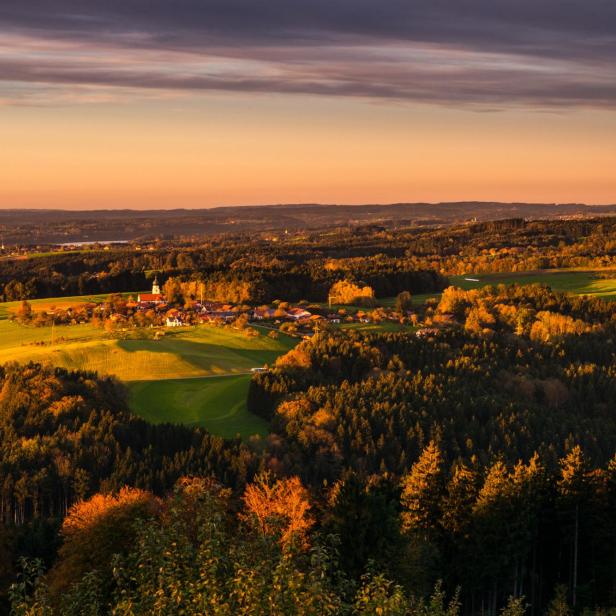 Landschaft mit Feldern, Wald und Dorf bei Sonnenuntergang mit orangefarbenem Himmel.