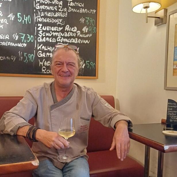 Wirt Franz Buchecker sitzt unter einer Tafel, auf der die Weinkarte zu sehen ist.