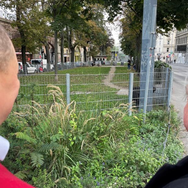 Zwei Männer blicken mit dem Rücken zur Kamera in eine Hundezone, wo sich zwei Menschen einen Schuss setzen.