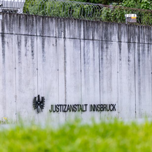 Eine graue Betonmauer mit Stacheldraht und der Aufschrift "Justizanstalt Innsbruck" ist zu sehen.