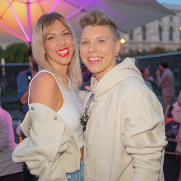 Zwei Frauen stehen eng beieinander und lachen in die Kamera