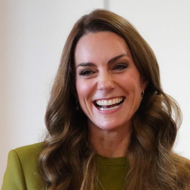 Lachende Prinzessin Kate mit gewellten Haaren trägt ein grünes Oberteil.