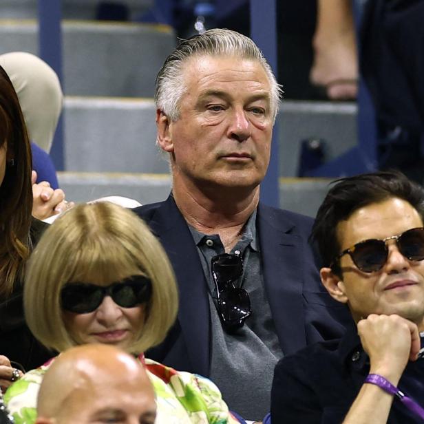 Alec Baldwin und Anna Wintour sitzen mit anderen Zuschauern auf einer Tribüne.
