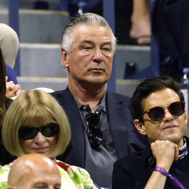 Alec Baldwin und Anna Wintour sitzen mit anderen Zuschauern auf einer Tribüne.