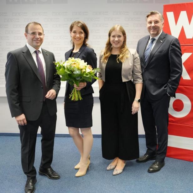 Vier Personen posieren vor einem roten WKO-Logo, eine Frau hält einen Blumenstrauß.