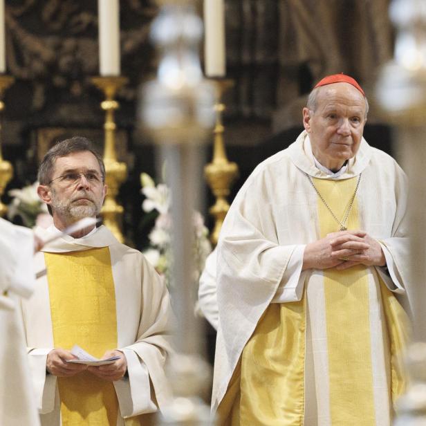 Josef Grünwidl und Christoph Schönborn. in weißen und gelben liturgischen Gewändern stehen in einer Kirche vor goldenen Kerzenhaltern.