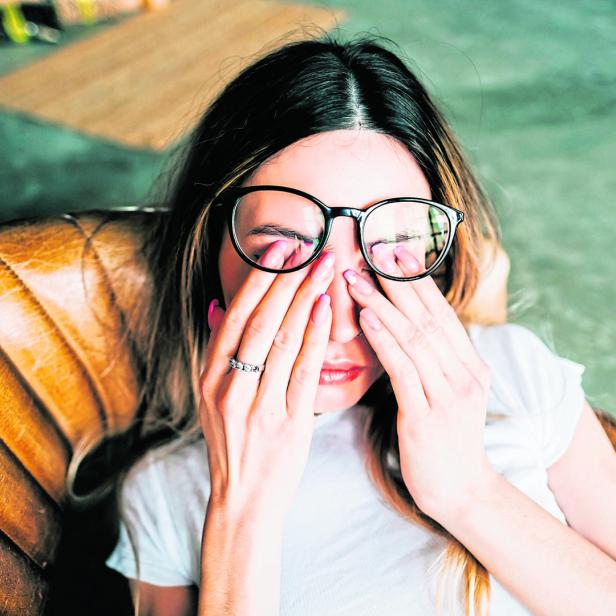 Young woman rubs her eyes after using glasses. Eye pain or fatigue concept.