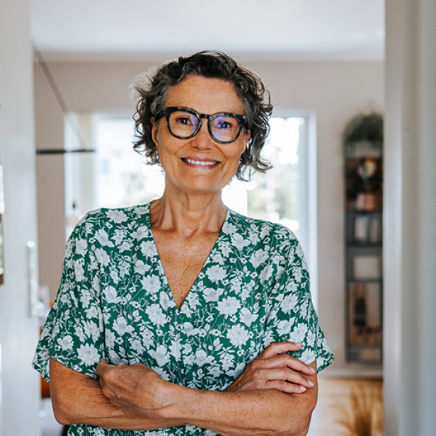 Eine Frau mit Brille steht in einem Flur und lächelt in die Kamera.