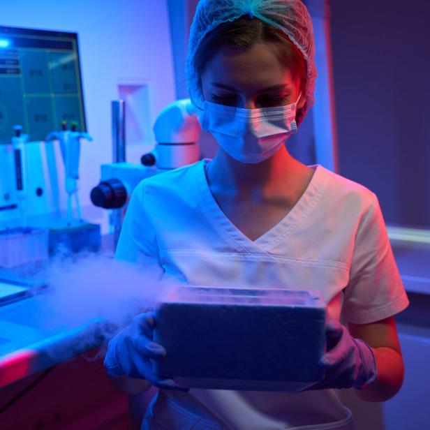 Woman embryologist holds tank with liquid nitrogen in her hands