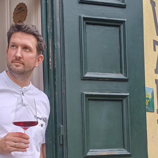Koch Werner Punz steht vor seinem Wirtshaus „Vinzenz Pauli“ mit einem Glas Rotwein in der Hand.