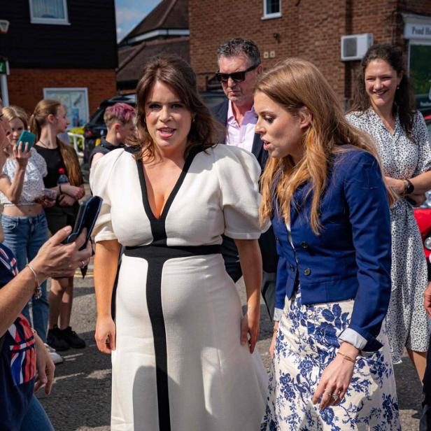 Prinzessin Eugenie in weißem Kleid und Prinzessin Beatrice in blau-weiß gemustertem Rock stehen im Freien.