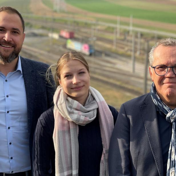 Drei Personen stehen auf einer Terrasse, im Hintergrund ist eine Lokomotive zu sehen.