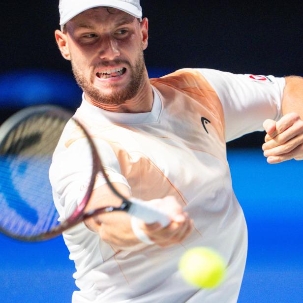 Ein Tennisspieler schlägt mit konzentriertem Gesichtsausdruck einen gelben Ball mit dem Schläger.