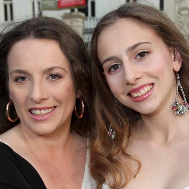 Zwei Frauen lächeln in die Kamera, eine mit goldenen Creolen und die andere mit auffälligen Ohrringen.