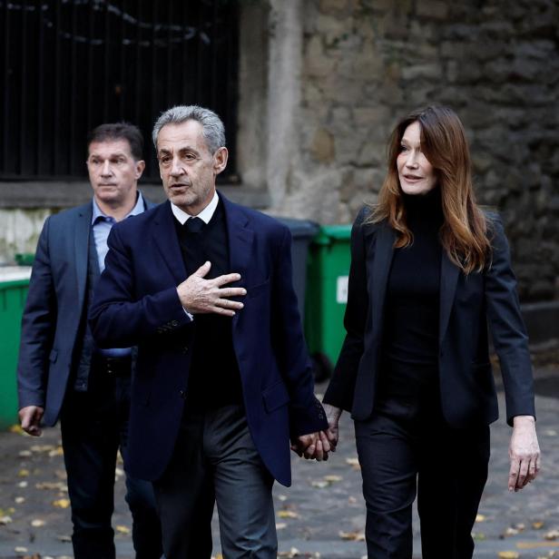 Nicolas Sarkozy und Carla Bruni gehen Händchen haltend, begleitet von einem Mann.