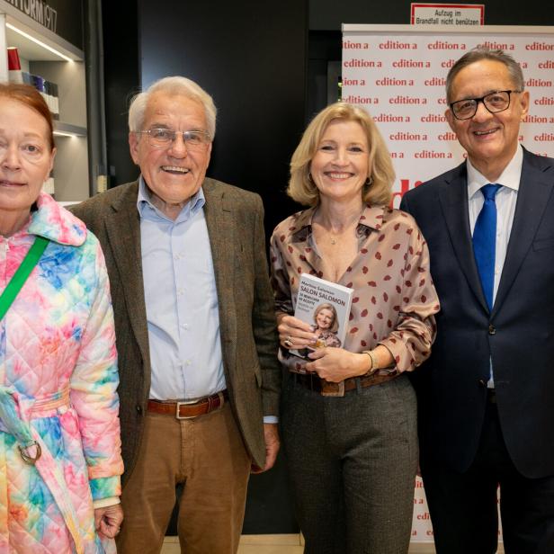 Vier Erwachsene stehen nebeneinander, eine Frau hält ein Buch und alle lächeln in einer Buchhandlung.