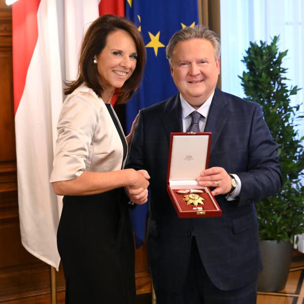 Eine Frau und ein Mann geben sich die Hand, der Mann hält eine geöffnete Schatulle mit einer Auszeichnung.