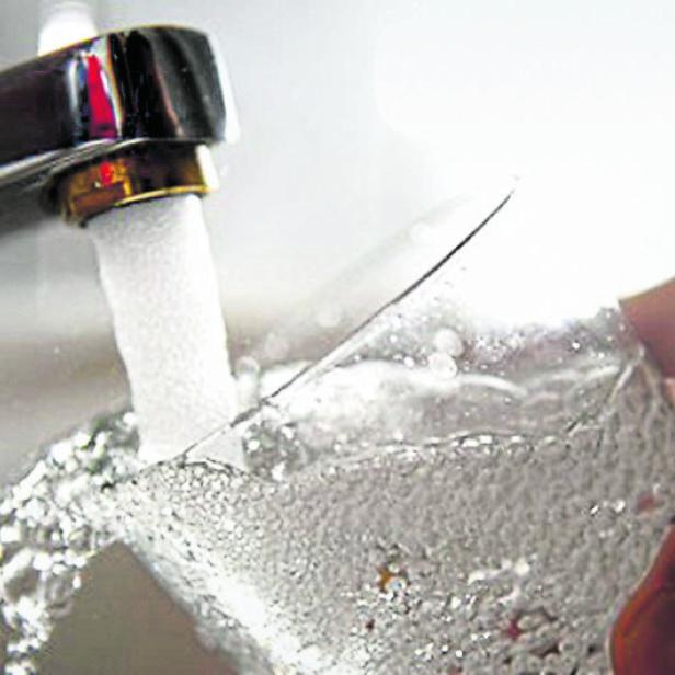 Wasser fließt aus einem Wasserhahn in ein Glas.