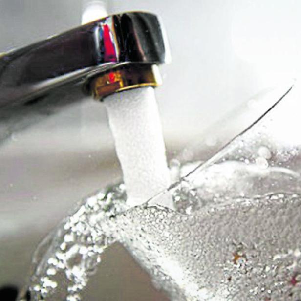 Wasser fließt aus einem Wasserhahn in ein Glas.