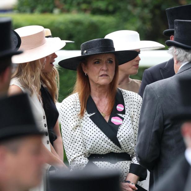 Sarah Ferguson, in einem gepunkteten Kleid und Hut, steht inmitten einer Menschenmenge mit Hüten und Anzügen.