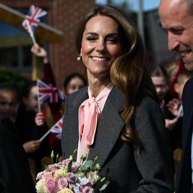 Kate, mit Blumenstrauß, lächelt neben William, während Kinder mit Union-Jack-Flaggen winken.