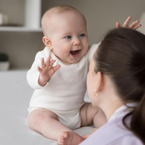 Ein Baby greift nach seiner Mutter, mit offenem Mund. // Ganzheitliche Baby-Balancing-Ausbildung von Iris Lichtenberger an der HOLFINITY Akademie stärkt Babys mit Kinesiologie und Cranio Sacral Techniken. 