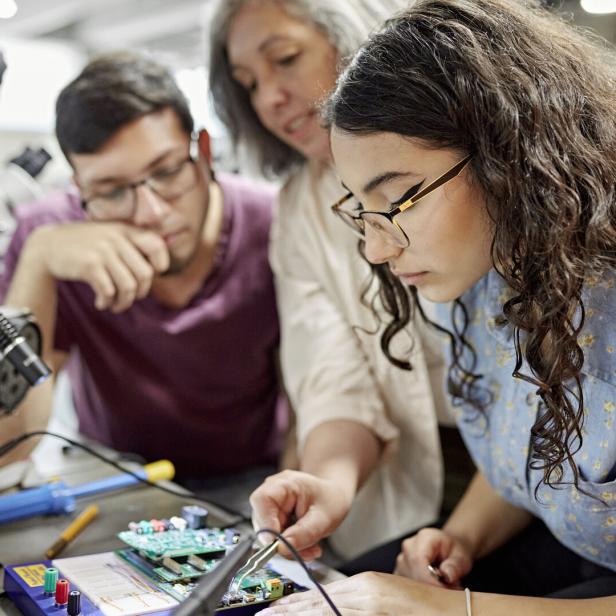 Lehrerin, die einer Studierenden bei der Elektrotechnik hilft.