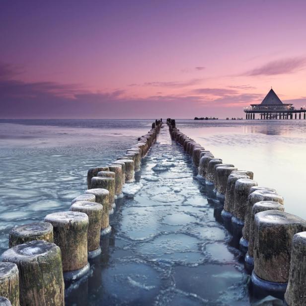 Ein Sonnenuntergang an einem Meer; mit Holzpfosten, die ins Wasser gehen