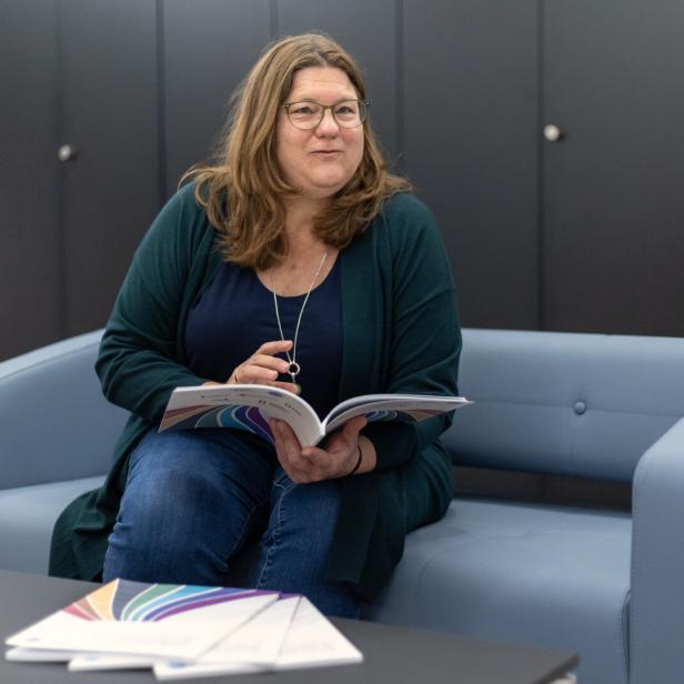 Margreth Keiler sitzt auf einer Couch mit aufgeschlagenem Bericht