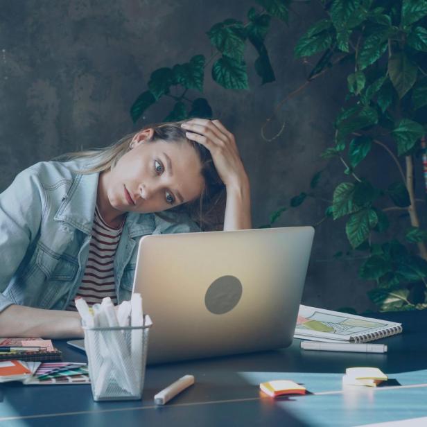 Frau sitzt erschöpft am Laptop am Arbeitsplatz