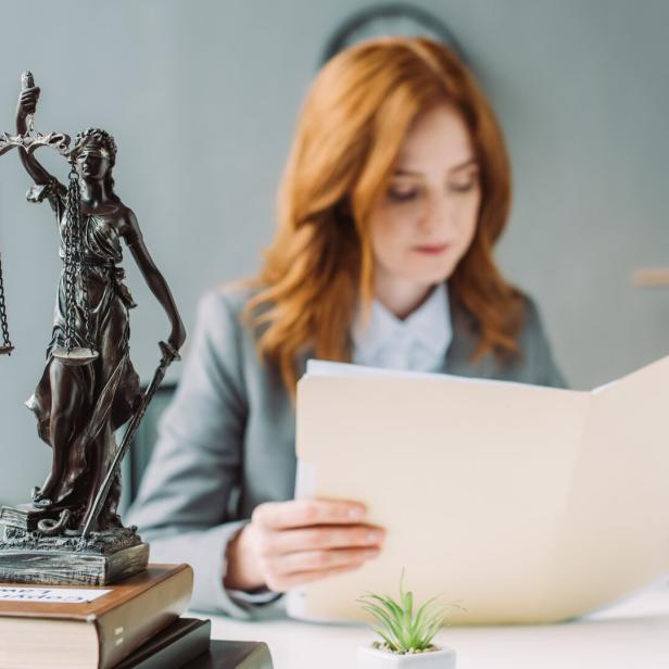 Female lawyer looking at folder, while sitting at workplace with themis figurine on pile of books on blurred background