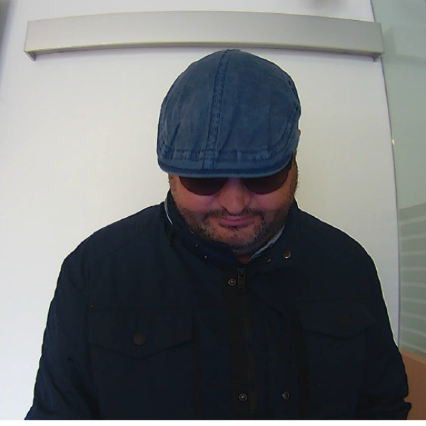 Eine Aufnahme von einer Bankomat-Kamera. Ein Mann mit blauer Kopfbedeckung und Sonnenbrille ist zu sehen.